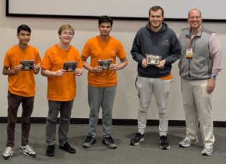 Binary Bears place first in regional programming competition Four young men in orange shirts hold plaques next to an older man in business casual attire, posing indoors.