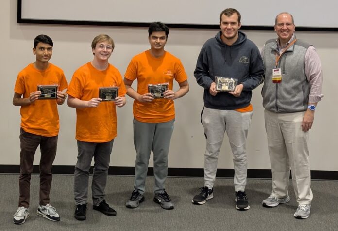 Binary Bears CCSC Four young men in orange shirts hold plaques next to an older man in business casual attire, posing indoors.