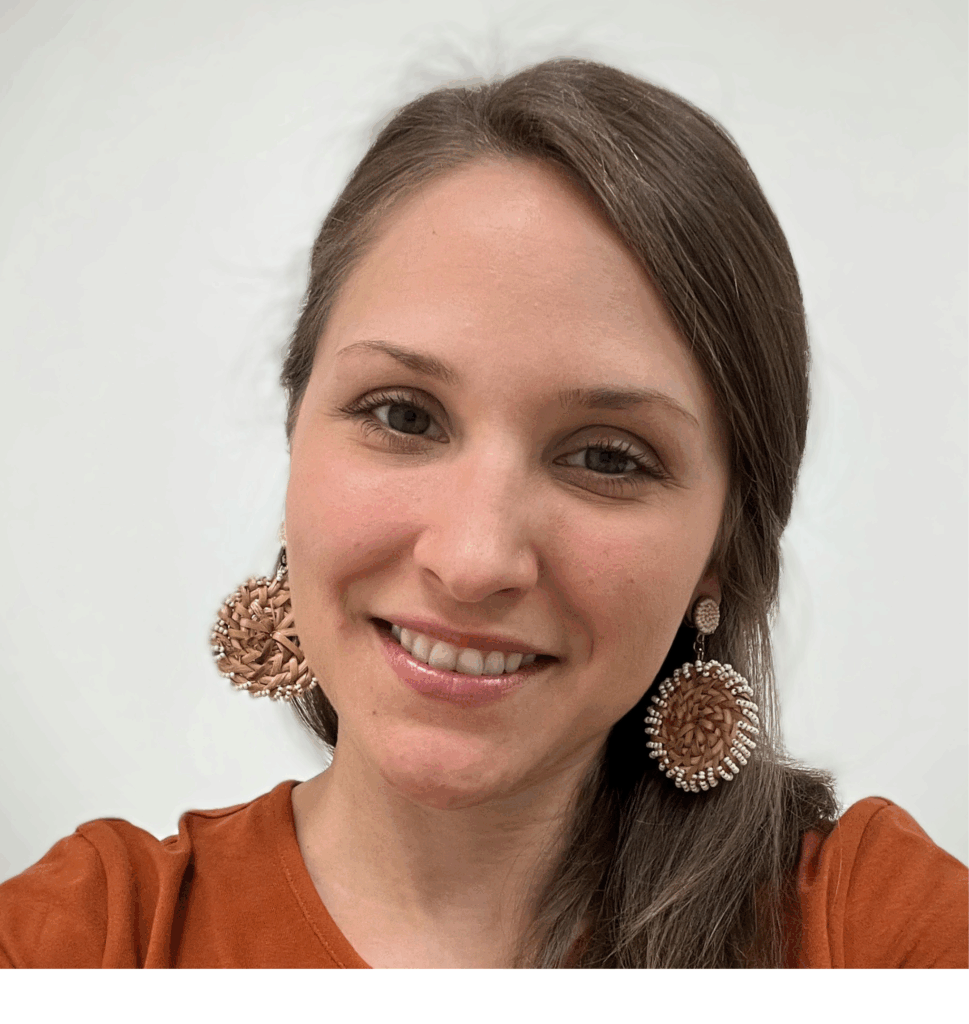 Woman with straight brown hair wearing large beaded earrings and an orange top, smiling at the camera against a plain background.