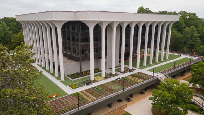 A modern, multi-story building with tall white columns and landscaped grounds, surrounded by trees.