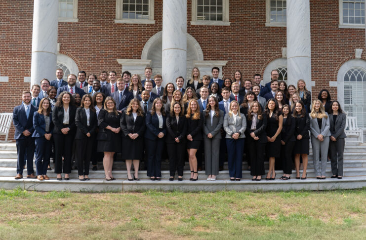A large group of professionally dressed people pose for a photo on outdoor steps in front of a brick building with columns.
