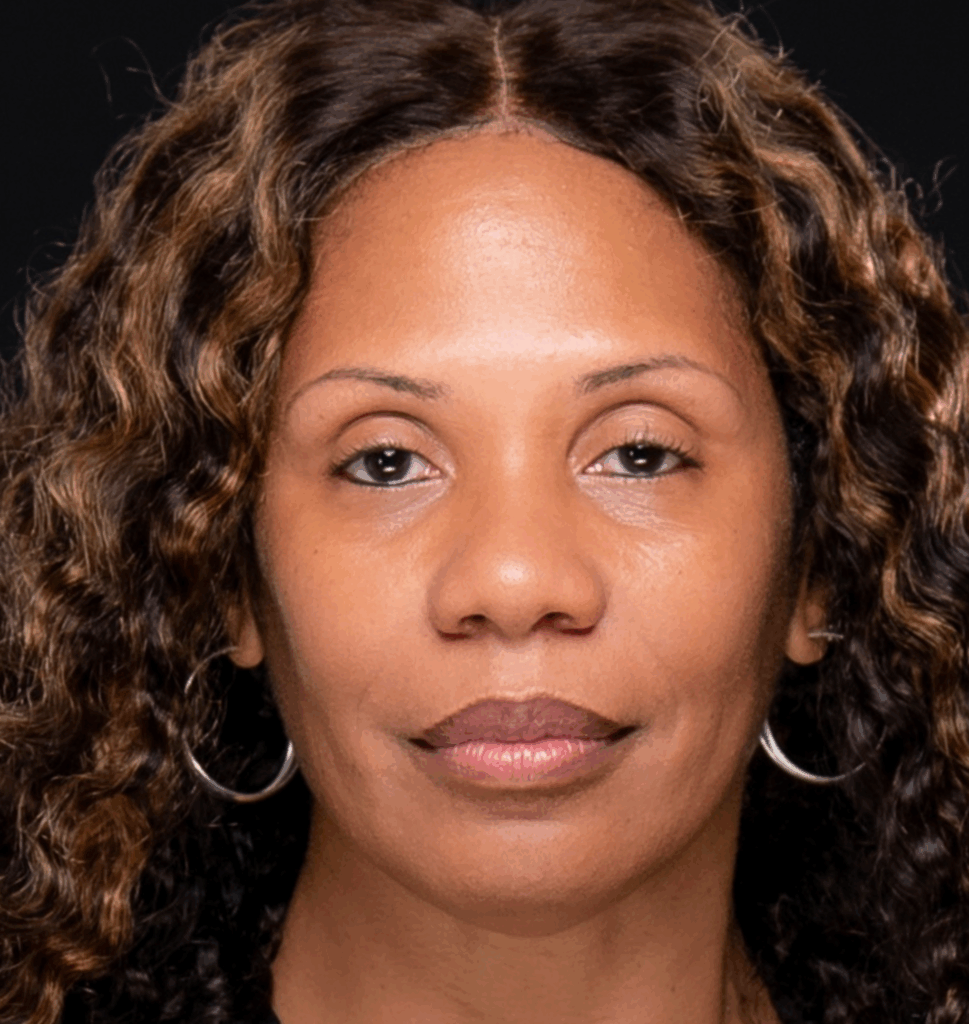 A woman with wavy brown hair and hoop earrings looks directly at the camera against a black background.
