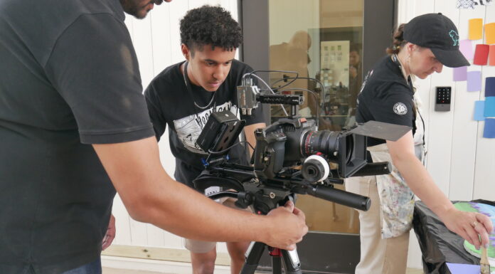 Mercer alumnus creates nonprofit for budding storytellers Three people set up and adjust a professional video camera mounted on a tripod indoors.