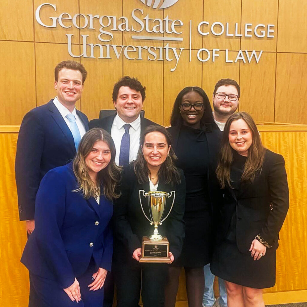 Seven people in business attire pose with a trophy at Georgia State University College of Law.