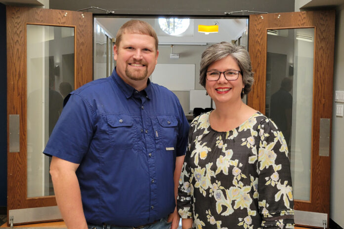 Dr. Justin Peterson and Glenda Grant stand smiling inside a building entrance with open wooden doors.