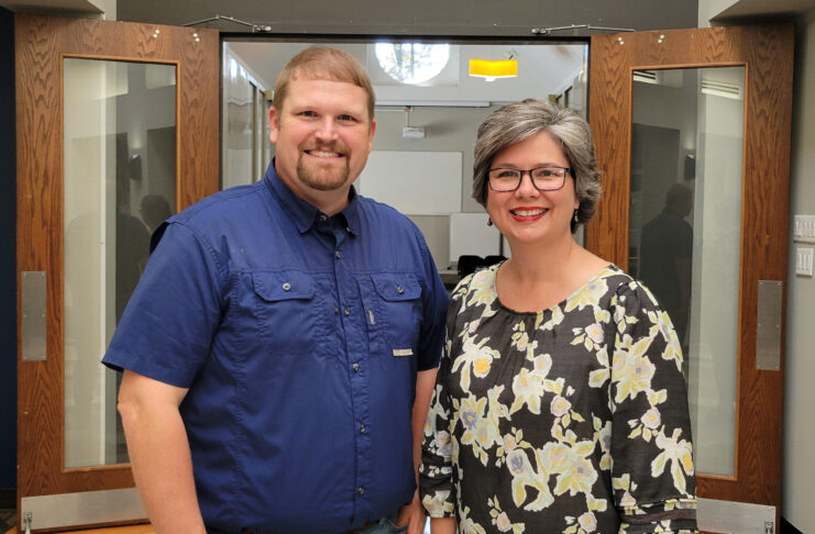 Dr. Justin Peterson and Glenda Grant stand smiling inside a building entrance with open wooden doors.