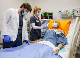 High-tech, real-life simulations prepare Mercer nursing students for practice Two Mercer nursing students practice patient care on a medical mannequin in a hospital room with monitoring equipment.