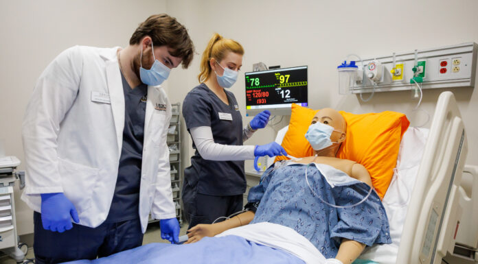 High-tech, real-life simulations prepare Mercer nursing students for practice Two Mercer nursing students practice patient care on a medical mannequin in a hospital room with monitoring equipment.