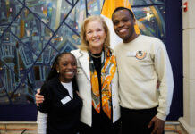 Mercer president seeks input on University’s future Mercer University President Dr. Penny L. Elkins and two students stand smiling together indoors in front of a colorful mural and a flag.
