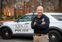 New Mercer Police deputy chief brings skill, expertise and compassion to role Deputy Chief Jeremy Robinson stands with arms crossed in front of a Mercer University Police vehicle parked on a tree-lined street.
