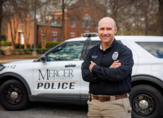 New Mercer Police deputy chief brings skill, expertise and compassion to role Deputy Chief Jeremy Robinson stands with arms crossed in front of a Mercer University Police vehicle parked on a tree-lined street.