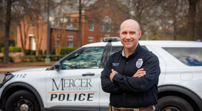 New Mercer Police deputy chief brings skill, expertise and compassion to role Deputy Chief Jeremy Robinson stands with arms crossed in front of a Mercer University Police vehicle parked on a tree-lined street.