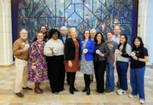 Mercer selected for Carnegie Foundation 2026 Community Engagement Classification Twelve people standing indoors in front of a colorful glass mural, some holding round white badges and smiling at the camera.