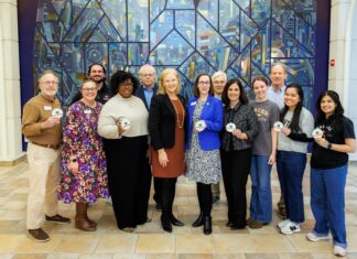 Mercer selected for Carnegie Foundation 2026 Community Engagement Classification Twelve people standing indoors in front of a colorful glass mural, some holding round white badges and smiling at the camera.