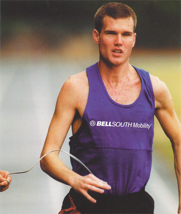 Tim Willis runs on a track, guided by a tether held by another person.