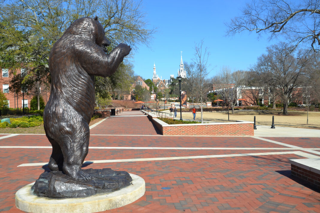 DSC_8181 A bronze bear statue stands on a brick plaza with campus buildings and trees in the background.