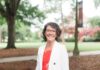 Emmilee Mitchell named interim associate vice president for financial planning Woman with short curly hair and glasses, wearing a white blazer, standing outdoors on a campus with trees in the background.