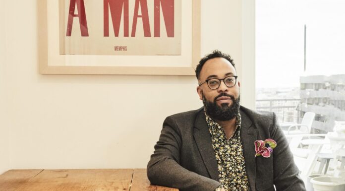 Center for Southern Studies to award 2026 Thomas Robinson Prize to poet, author Kevin Young A man with glasses sits at a wooden table beneath a framed sign that reads I AM A MAN in bold red letters.