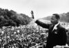 Dr. Joseph M. Hendricks Center for Campus Initiatives to host commemorative program honoring life and legacy of Dr. Martin Luther King Jr. A man in a suit waves to a large crowd gathered outdoors during a historic civil rights demonstration.