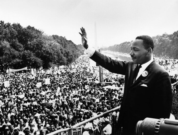 Martin Luther King Jr. waves to a large crowd gathered outdoors during a historic civil rights demonstration.
