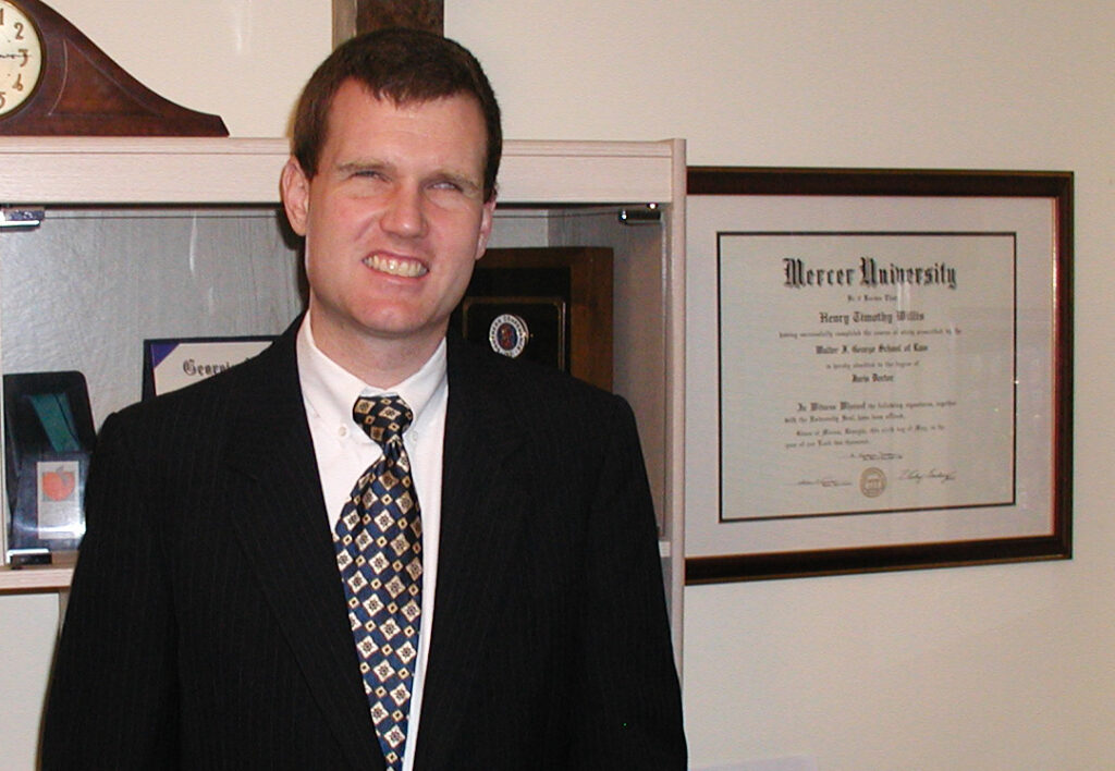 Tim Willis stands next to his diploma from Mercer University hanging on the wall.