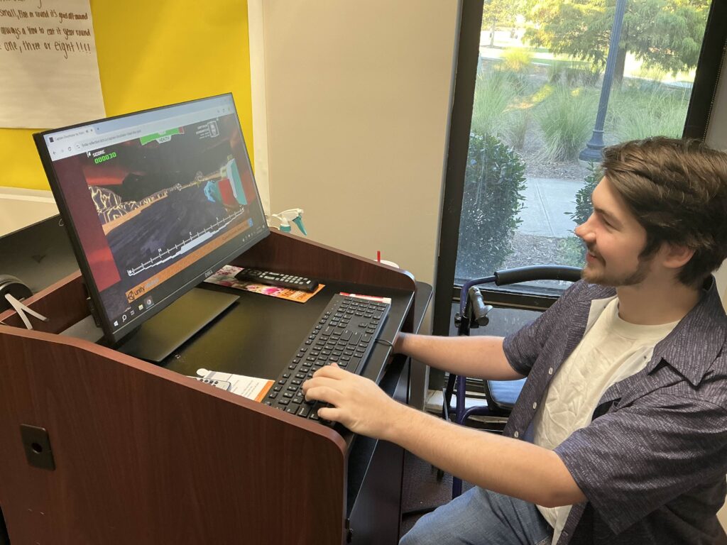 A young man sits at a desk using a computer, looking at a video with animals on the screen.