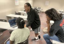 Mercer club provides space for video game creation Three people in a classroom look at code on a laptop, with one person standing and talking while others sit.