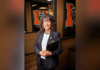 President Elkins appoints Dr. Maria Hammett as interim senior vice president for enrollment management A woman in business attire holds a clipboard, standing in an office with bear logos on glass walls behind her.