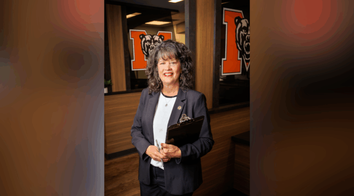 President Elkins appoints Dr. Maria Hammett as interim senior vice president for enrollment management A woman in business attire holds a clipboard, standing in an office with bear logos on glass walls behind her.