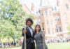Mercer senior wants to inspire leadership, resilience in others Two people in formal attire holding ceremonial staffs stand outside a large brick academic building, with a crowd behind them.
