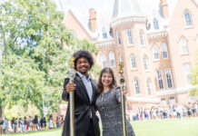 Mercer senior wants to inspire leadership, resilience in others Two people in formal attire holding ceremonial staffs stand outside a large brick academic building, with a crowd behind them.