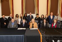 Mercer and Georgia Public Safety Training Center partner to strengthen training and educational opportunities Seventeen people, some seated and some standing, pose for a formal group photo in a conference room with gold curtains.