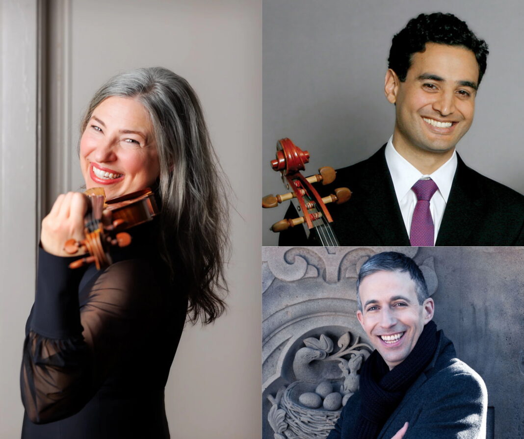 A woman holding a violin and smiling is on the left, with two men smiling on the right, one holding a violin scroll.