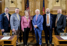 School of Medicine receives over $600,000 to continue fighting opioid epidemic Six people in business attire stand together in a government chamber with flags and wooden desks visible in the background.