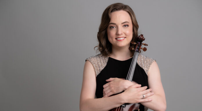 McDuffie Center for Strings welcomes alumna Emily Brandenburg as new director Woman in a black dress holding a violin and smiling, standing in front of a plain gray background.
