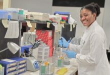 Pharmacy student awarded predoctoral fellowship for hypertension research Emmanuella Ezewudo in a lab coat uses a pipette at a laboratory bench with various scientific equipment and supplies.