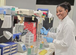 Pharmacy student awarded predoctoral fellowship for hypertension research Emmanuella Ezewudo in a lab coat uses a pipette at a laboratory bench with various scientific equipment and supplies.