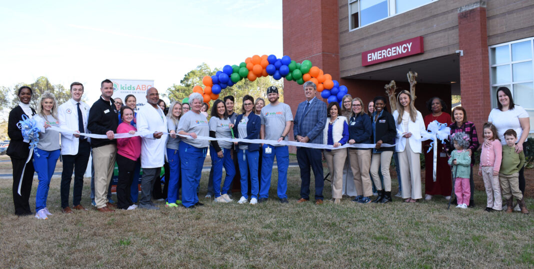 Wayne Memorial KidsABC Ribbon Cutting A group of people stand in front of an emergency room entrance, holding a ribbon for a ribbon-cutting ceremony.