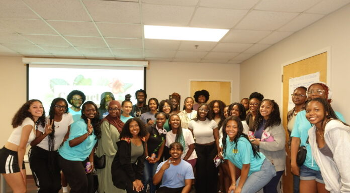 CaribSA provides space for community, cultural immersion A group of people pose together and smile in a classroom with a presentation projected on the wall behind them.