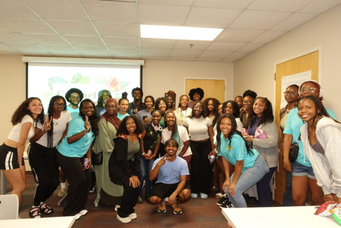 A group of people pose together and smile in a classroom with a presentation projected on the wall behind them.