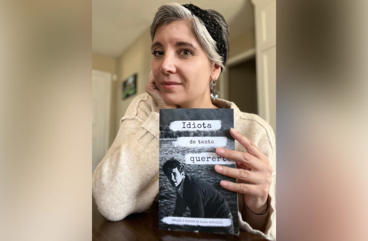 Dr. Clara Mengolini holds a book titled Idiota de tanto quererte and looks at the camera.