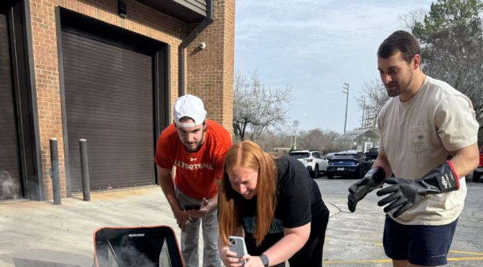 Cookstove project provides students with new perspective on engineering Three people observe and record an experiment with a smoking container on cinder blocks in a parking lot.