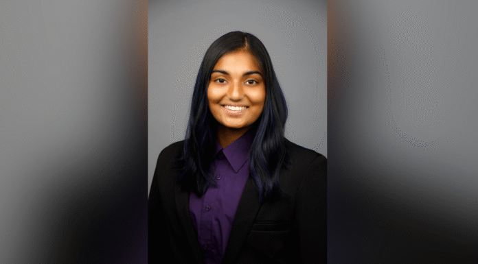 Sophomore awarded Fulbright Canada-Mitacs Globalink Research Internship A person with long dark hair, wearing a black blazer and purple shirt, smiles at the camera against a gray background.