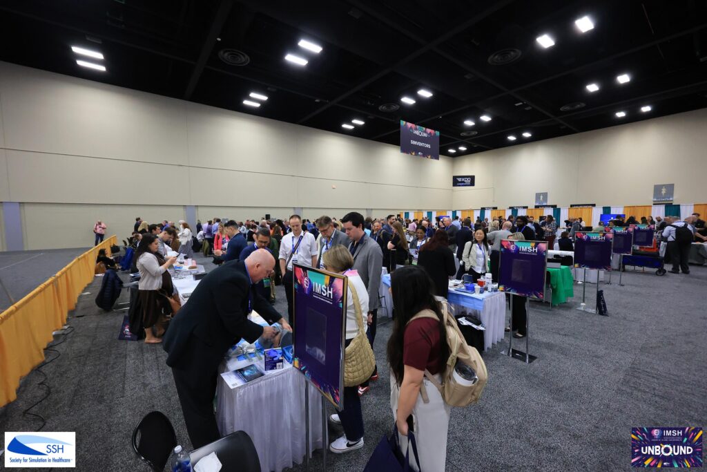 People gather around booths and tables at a professional conference inside a large, well-lit convention hall.