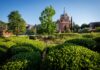 Faculty and Staff Notables | April 2026 Red brick university building with a clock tower, surrounded by green shrubs and trees under a clear blue sky.