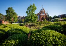 Faculty and Staff Notables | April 2026 Red brick university building with a clock tower, surrounded by green shrubs and trees under a clear blue sky.