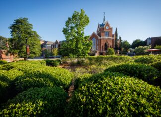 Faculty and Staff Notables | April 2026 Red brick university building with a clock tower, surrounded by green shrubs and trees under a clear blue sky.