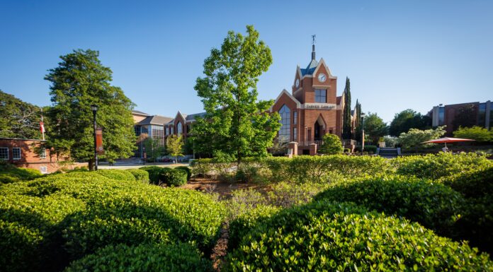 Faculty and Staff Notables | April 2026 Red brick university building with a clock tower, surrounded by green shrubs and trees under a clear blue sky.