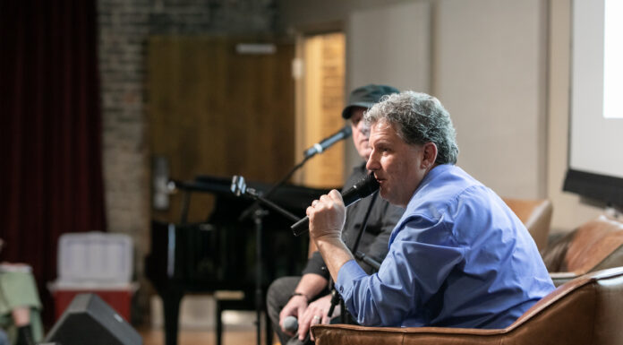 Music producer’s album pays homage to Mercer heritage, American heroes Man in a blue shirt speaks into a microphone while seated on a stage during an indoor event.