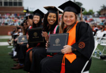Mercer recognized for fostering student success from enrollment to post-graduation Mercer graduates in caps and gowns sit in rows holding diplomas during an outdoor graduation ceremony.